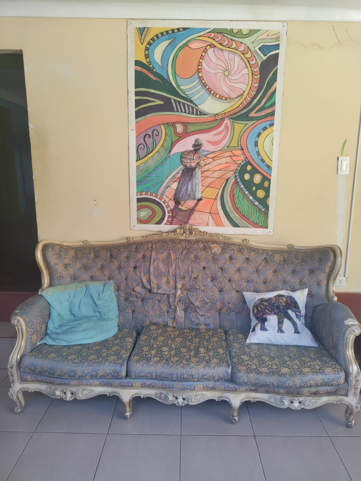 A vintage sofa with a patterned cushion and a decorative pillow, positioned in front of a colorful abstract painting on the wall.