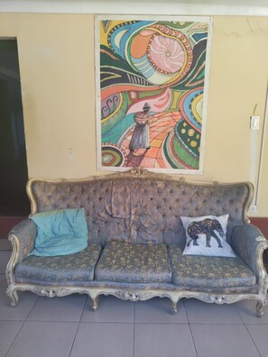 A vintage sofa with a patterned cushion and a decorative pillow, positioned in front of a colorful abstract painting on the wall. - Aguaymanto Hostel (Pisac)