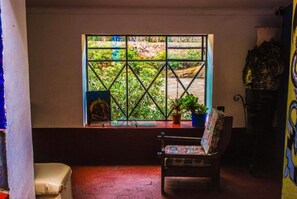 A room with a window, a chair, and a small table with a plant. - Aguaymanto Hostel (Pisac)