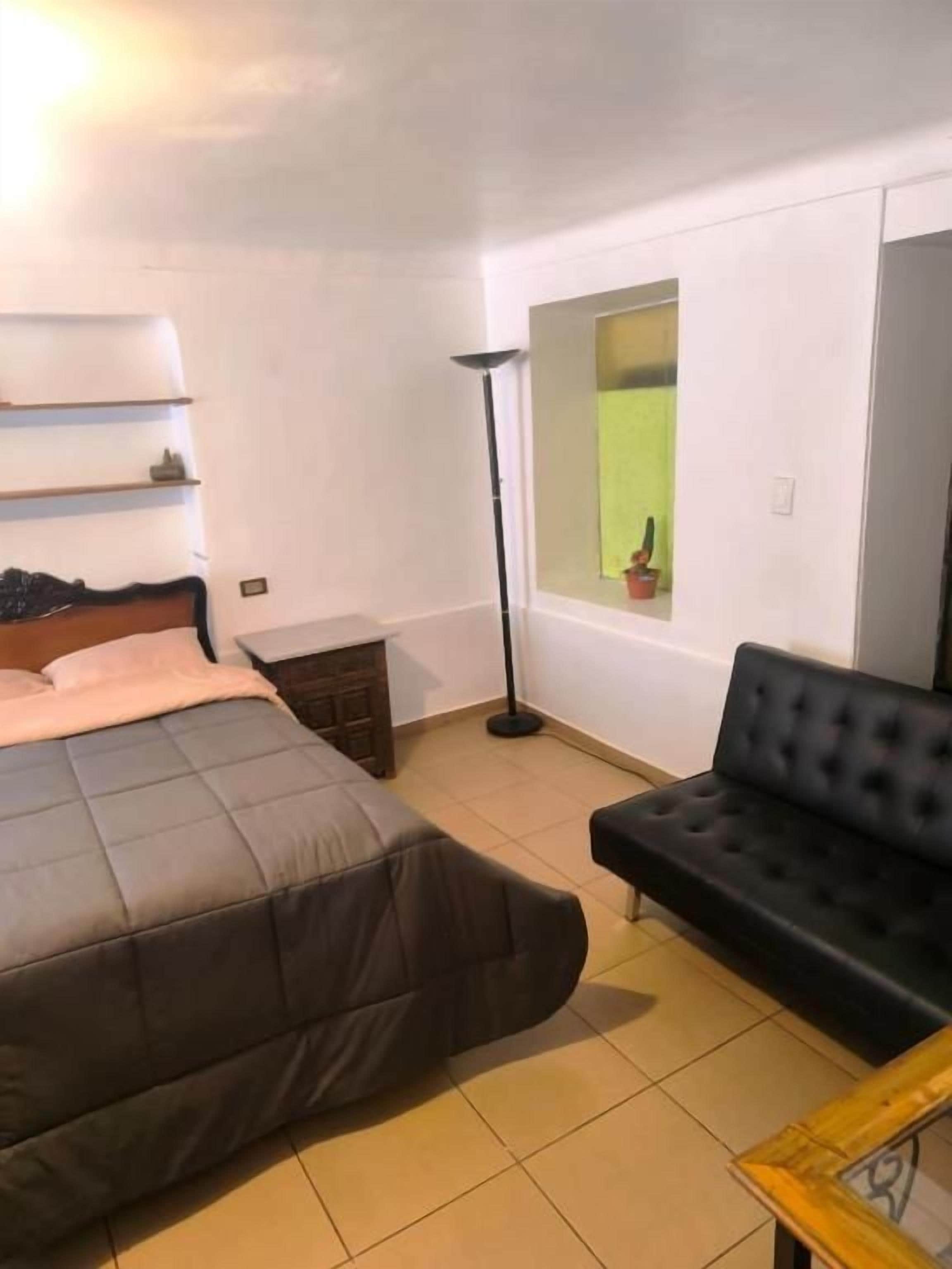 Een slaapkamer met een bed, een zwarte bank, een vloerlamp en een raam met uitzicht.