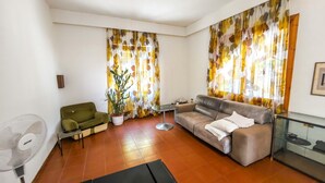 A living room with a sofa, a green armchair, a floor fan, and a potted plant.