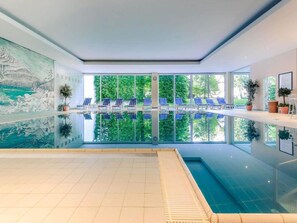 An indoor swimming pool with a clear view of the outdoors, blue lounge chairs, and potted plants. - 2 Person Holiday Park Home in Garmisch-partenkirchen (Garmisch-Partenkirchen)