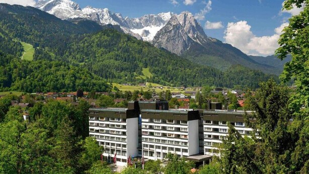 A hotel with multiple floors, surrounded by lush greenery and mountains in the background. - 2 Person Holiday Park Home in Garmisch-partenkirchen (Garmisch-Partenkirchen)