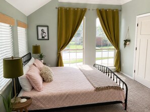 A bedroom with a bed, a bedside lamp, a window with curtains, and a framed picture on the wall. - OKC 1 Bed 1 Bath Mini Guesthouse - The Margot (Oklahoma City)