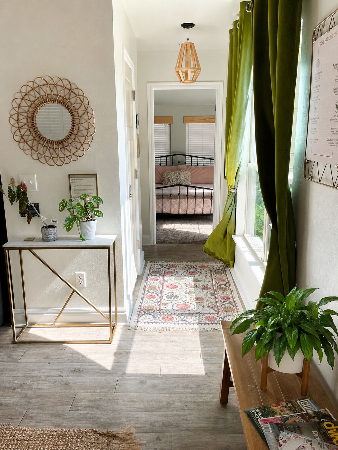 A hallway with a bed, a mirror, a hanging light fixture, and a green curtain.