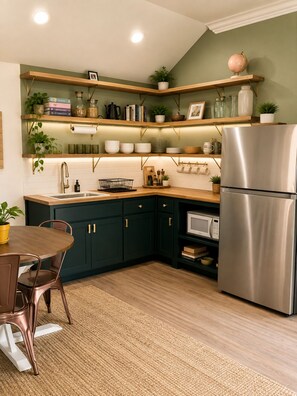 A kitchen with dark green cabinets, wooden shelves, and a stainless steel refrigerator. - OKC 1 Bed 1 Bath Mini Guesthouse - The Margot (Oklahoma City)