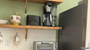 Ett kök med en mikrovågsugn, brödrost och kaffebryggare på bänkskivan, ett kylskåp och en hylla med dekorativa föremål.