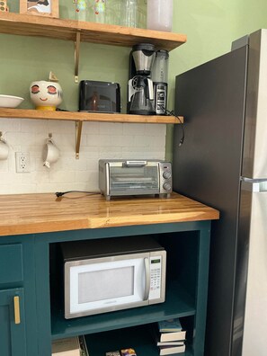 Eine Küche mit Mikrowelle, Toaster und Kaffeemaschine auf der Arbeitsplatte, einem Kühlschrank und einem Regal mit Dekoration.