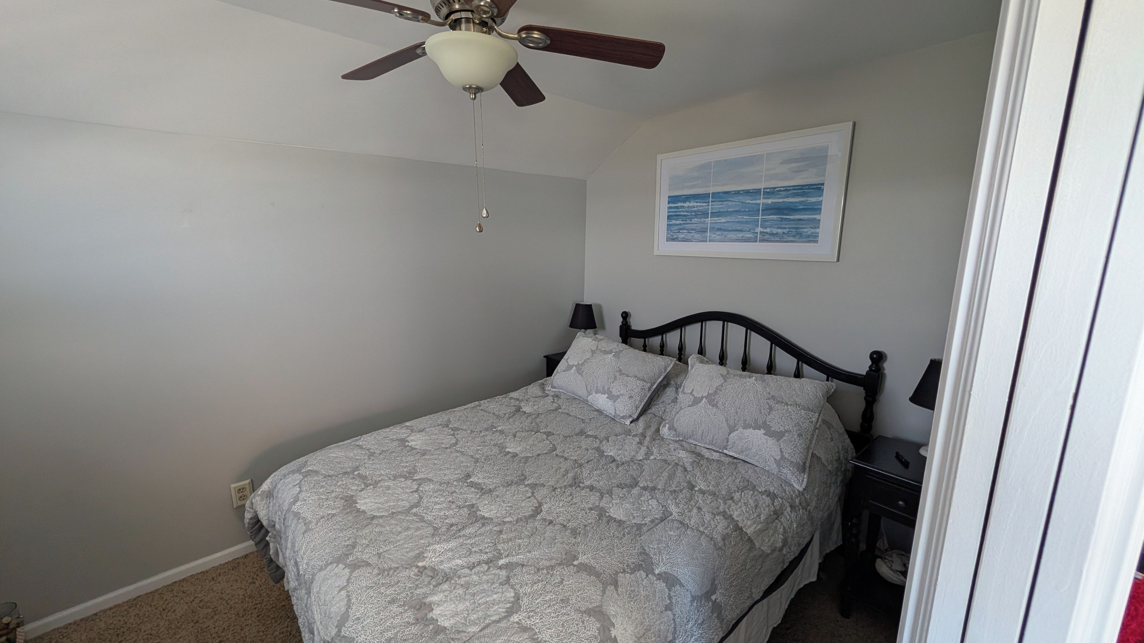 A bedroom with a bed, a ceiling fan, a nightstand, a lamp, and a framed picture on the wall.