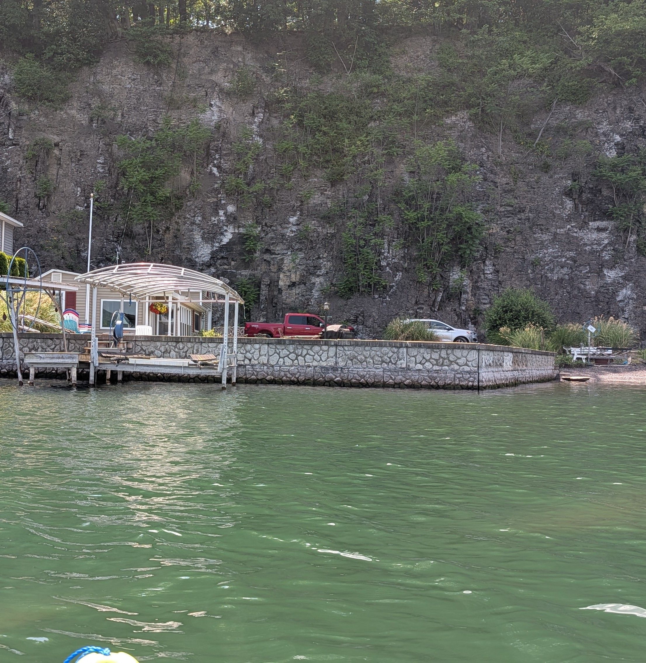 A waterfront property with a dock, a covered seating area, and a stone wall.