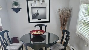 A dining area with a round table, four chairs, a chandelier, a framed picture, and a potted plant.