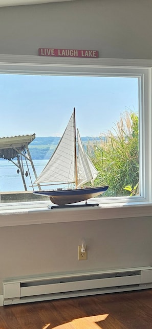 Un modelo de velero en un alféizar con vista a un lago y un cartel que dice 'LIVE LAUGH LAKE'.