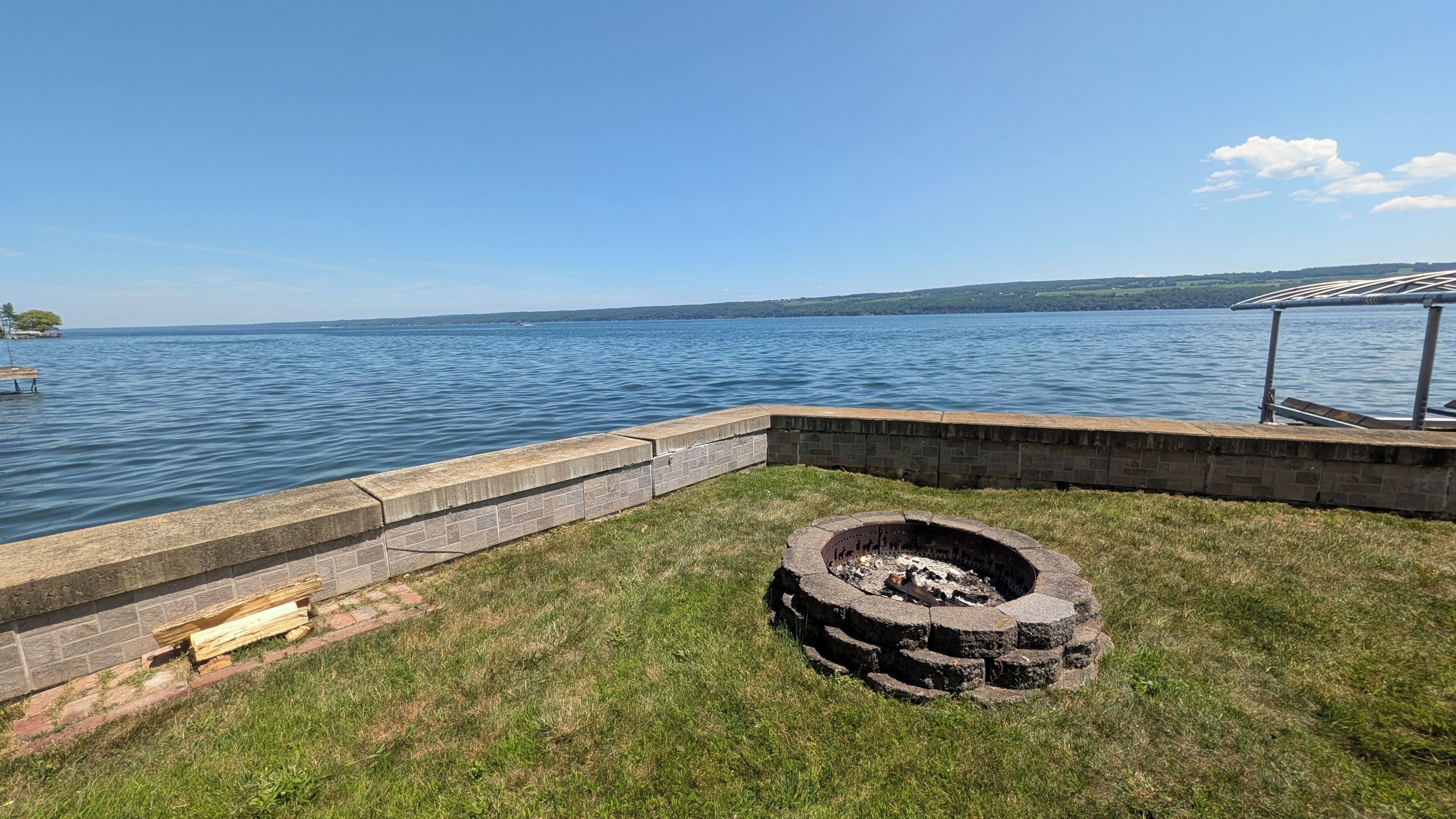 Une terrasse au bord du lac, avec un foyer et un mur de pierre donnant sur l’eau.
