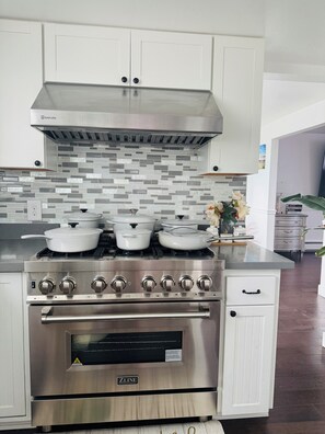 A kitchen with a stainless steel stove, white cabinets, and a tiled backsplash.