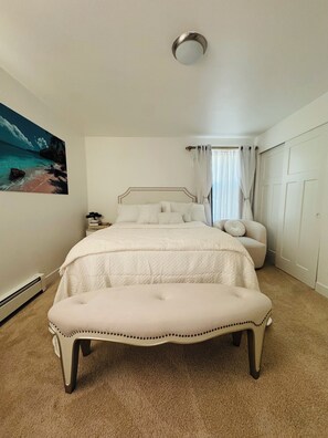 A bedroom with a bed, a bench, a painting, and a wardrobe.