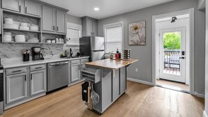 A kitchen with grey cabinets, a wooden countertop, and a view to the outside.
