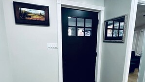 A hallway with a black door, a framed picture on the wall, and a trash bin.