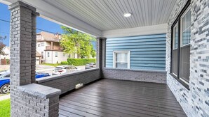 A covered porch with a brick column, a blue exterior wall, and a view of a residential street.