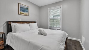 A bedroom with a bed, a ceiling fan, a window with blinds, and a framed picture on the wall.
