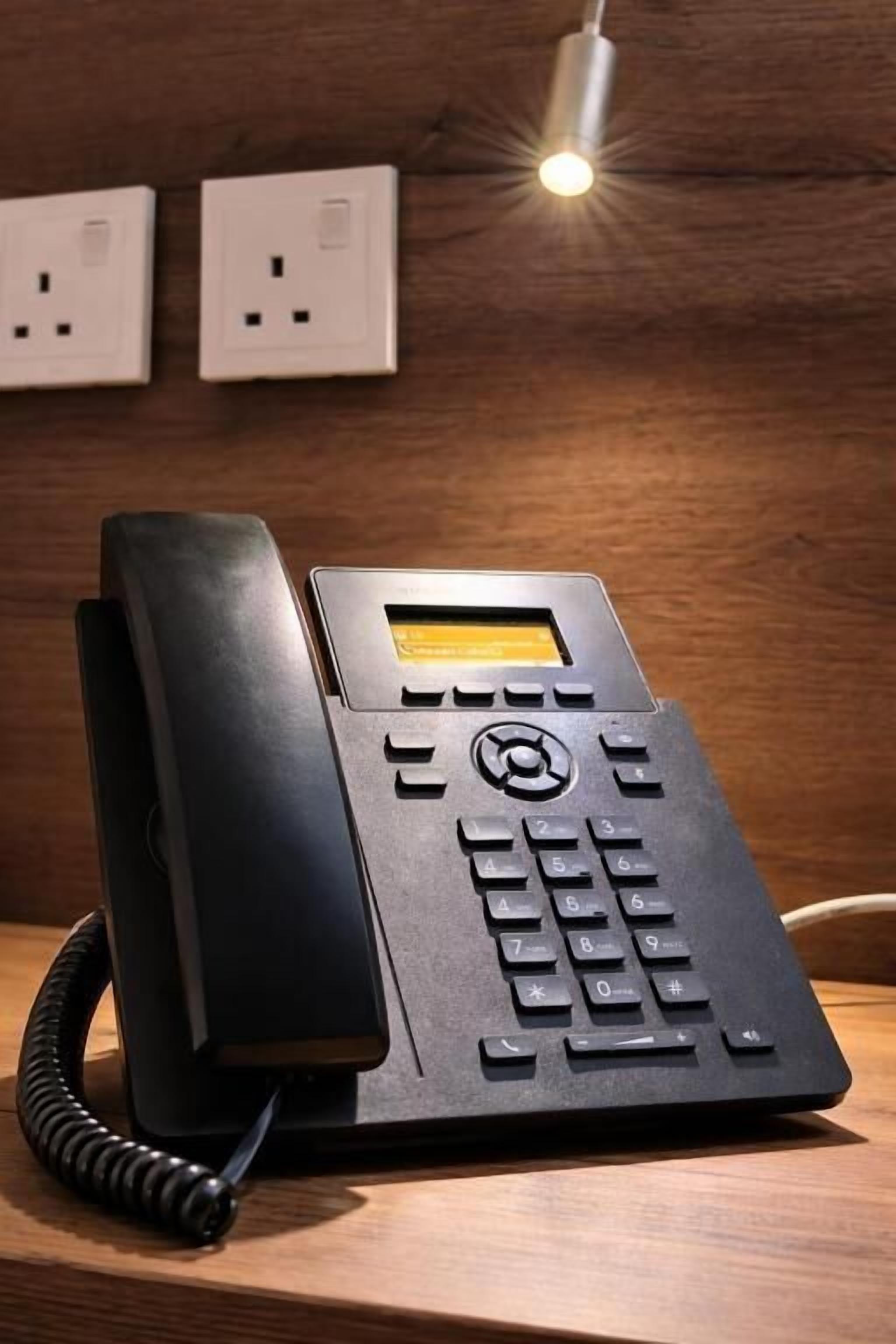 Ein schwarzes Telefon mit Tastenfeld und kleinem Bildschirm, auf einer Holzfläche platziert.