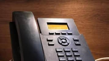 Ein schwarzes Telefon mit Tastenfeld und kleinem Bildschirm, auf einer Holzfläche platziert.