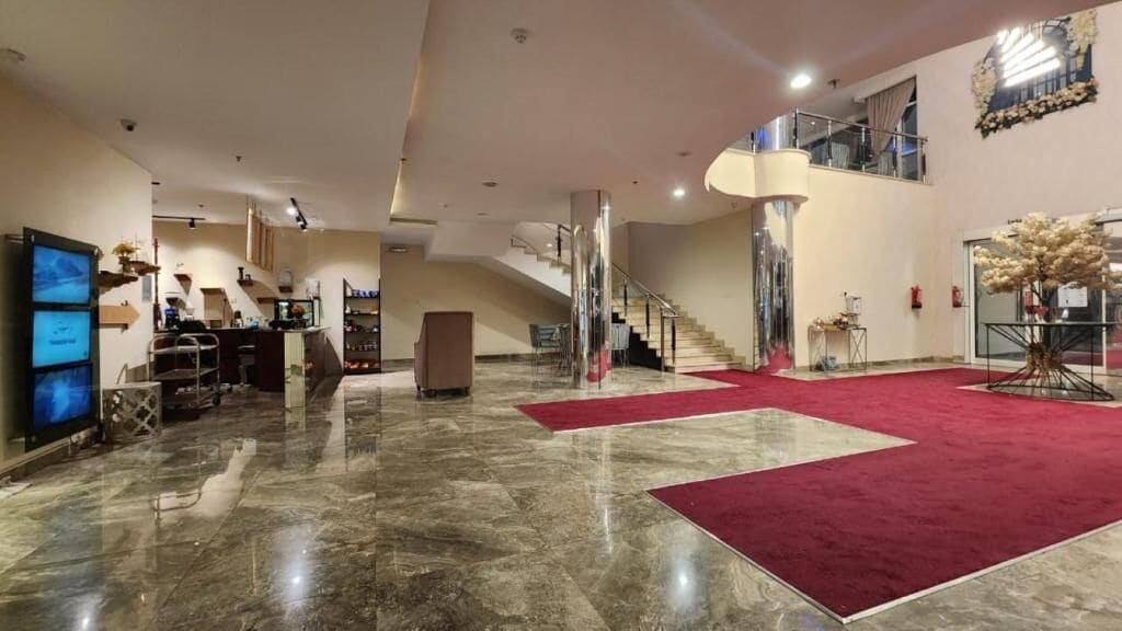 Un vestíbulo espacioso con piso de mármol, alfombra roja, una escalera y una pantalla grande.