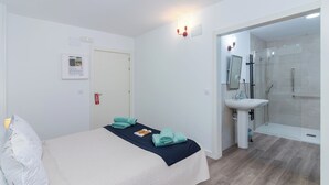 Ett hotellrum med en säng, ett badrum med handfat och dusch samt en dörr som leder till ett annat rum.