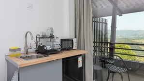 Ett litet, praktiskt kök med en diskho, en kaffemaskin och ett torkställ för disken. Det finns ett litet bord med en stol, och utsikten sträcker sig utåt genom en balkong med ett räcke.