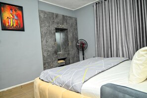 Ein Schlafzimmer mit Bett, Nachttisch, Spiegel, Ventiliator und einem Bild an der Wand.