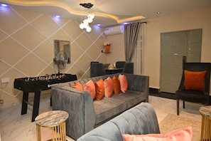 A living room with a sofa, armchairs, a foosball table, and a dining area. - Luxury 3BR Apartment off Toyin Str | 3 Queen Beds (Lagos)