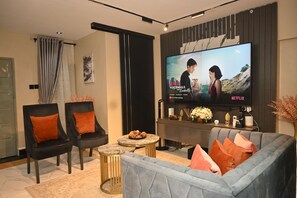 Ein modernes Wohnzimmer mit Flachbildfernseher, zwei schwarzen Sessel, einem grauen Sofa und einem Couchtisch.