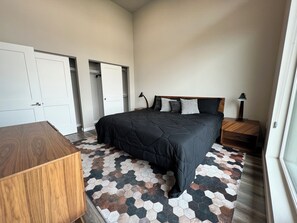 Ein Schlafzimmer mit einem großen Bett, einem Nachttisch aus Holz, einem Schreibtisch und einem Kleiderschrank mit Schiebetüren.