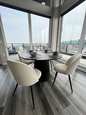 A modern dining area with a round table, four chairs, and a view of the cityscape through large windows. - Penthouse 2-bed with Spokane’s best views! Building amenities included. (Spokane)