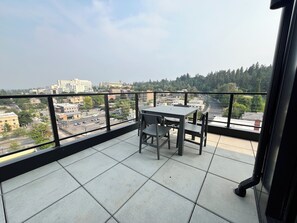 Ein Balkon mit Tisch und Stühlen, der einen Blick auf eine Stadt mit Gebäuden und Bäumen bietet.