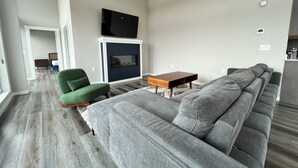 Ett modernt vardagsrum med en hörnsoffa, en grön fåtölj, ett soffbord i trä och en platt-TV som är monterad på väggen.