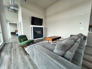 Ein modernes Wohnzimmer mit einem Ecksofa, einem grünen Sessel, einem Holztisch und einem flachbildfernseher an der Wand.