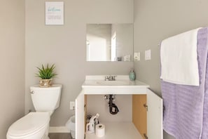 A bathroom with a toilet, sink, mirror, and towel rack.
