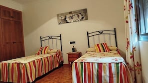 A bedroom with two single beds, a wooden wardrobe, a nightstand, and a wall-mounted painting. - Casa Miranda Cómpeta by Ruralidays (Málaga)