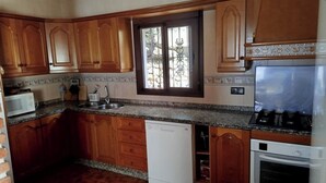 A kitchen with wooden cabinets, a built-in dishwasher, a microwave, a sink, and a stove. - Casa Miranda Cómpeta by Ruralidays (Málaga)