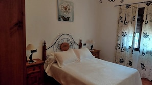 A bedroom with a bed, two bedside tables with lamps, a wooden headboard, a wall-mounted painting, and patterned curtains. - Casa Miranda Cómpeta by Ruralidays (Málaga)