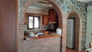 A kitchen with a brick archway, wooden cabinets, a stove, and a refrigerator. - Casa Miranda Cómpeta by Ruralidays (Málaga)