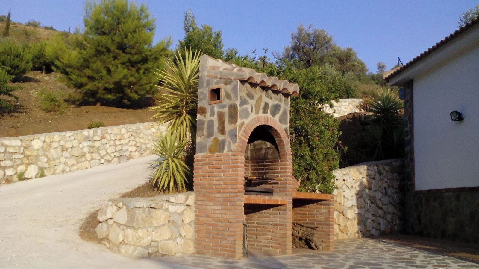 A stone and brick outdoor oven structure with a small opening, surrounded by a stone wall and vegetation.