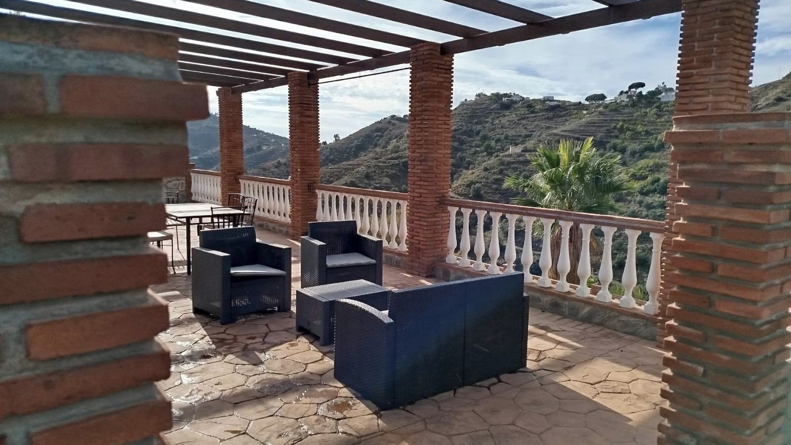 Un patio al aire libre con mobiliario de mimbre y vistas a un paisaje montañoso.