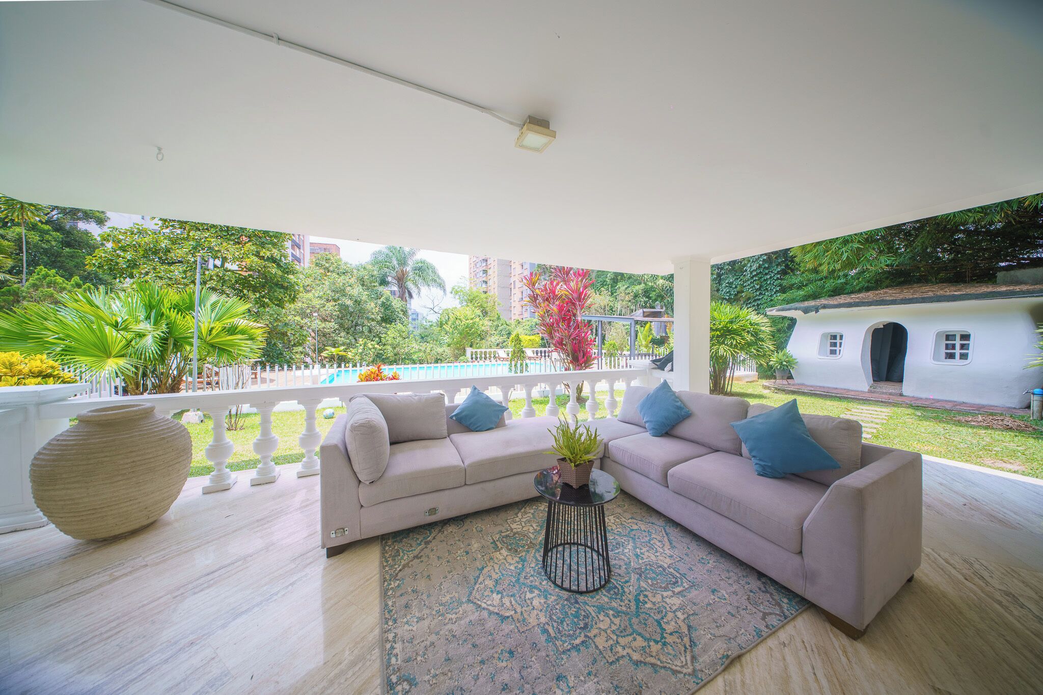 A modern living room with a beige sofa, a round coffee table, and a view of a pool and greenery.