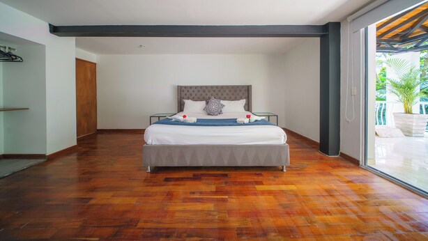 A spacious bedroom with a large bed, a wooden floor, and a view of greenery through a glass door. - The Garden Mansion | 11 Bedrooms with Club Lounge•Jacuzzi•Olympic Pool•Maid•AC (Medellín)
