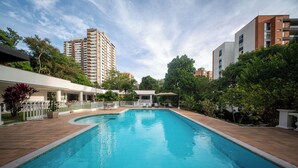 A swimming pool with a tiled deck, surrounded by greenery and buildings. - The Garden Mansion | 11 Bedrooms with Club Lounge•Jacuzzi•Olympic Pool•Maid•AC (Medellín)