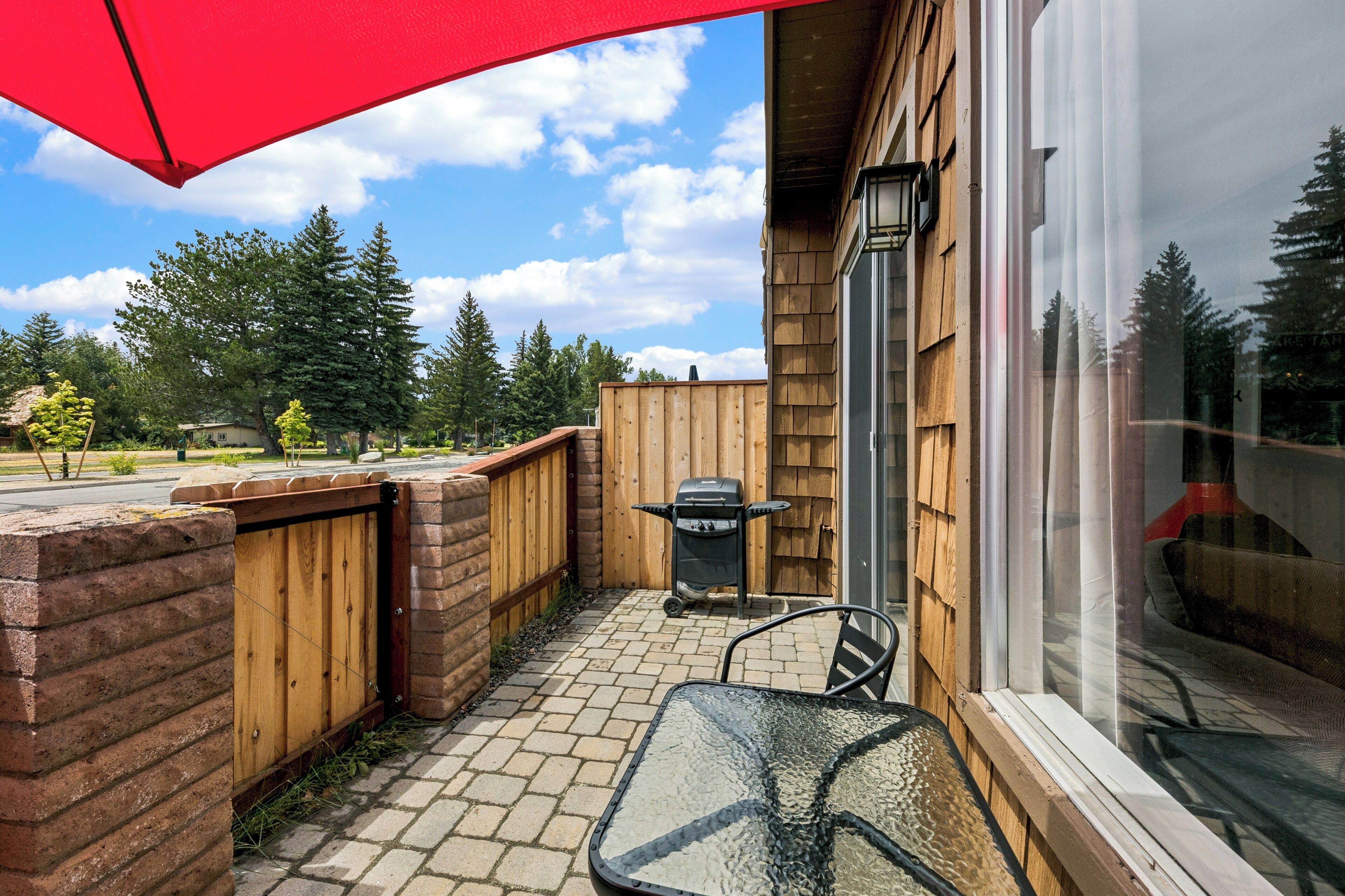 A patio with a table and chairs, a wooden fence, and a view of trees and a street.