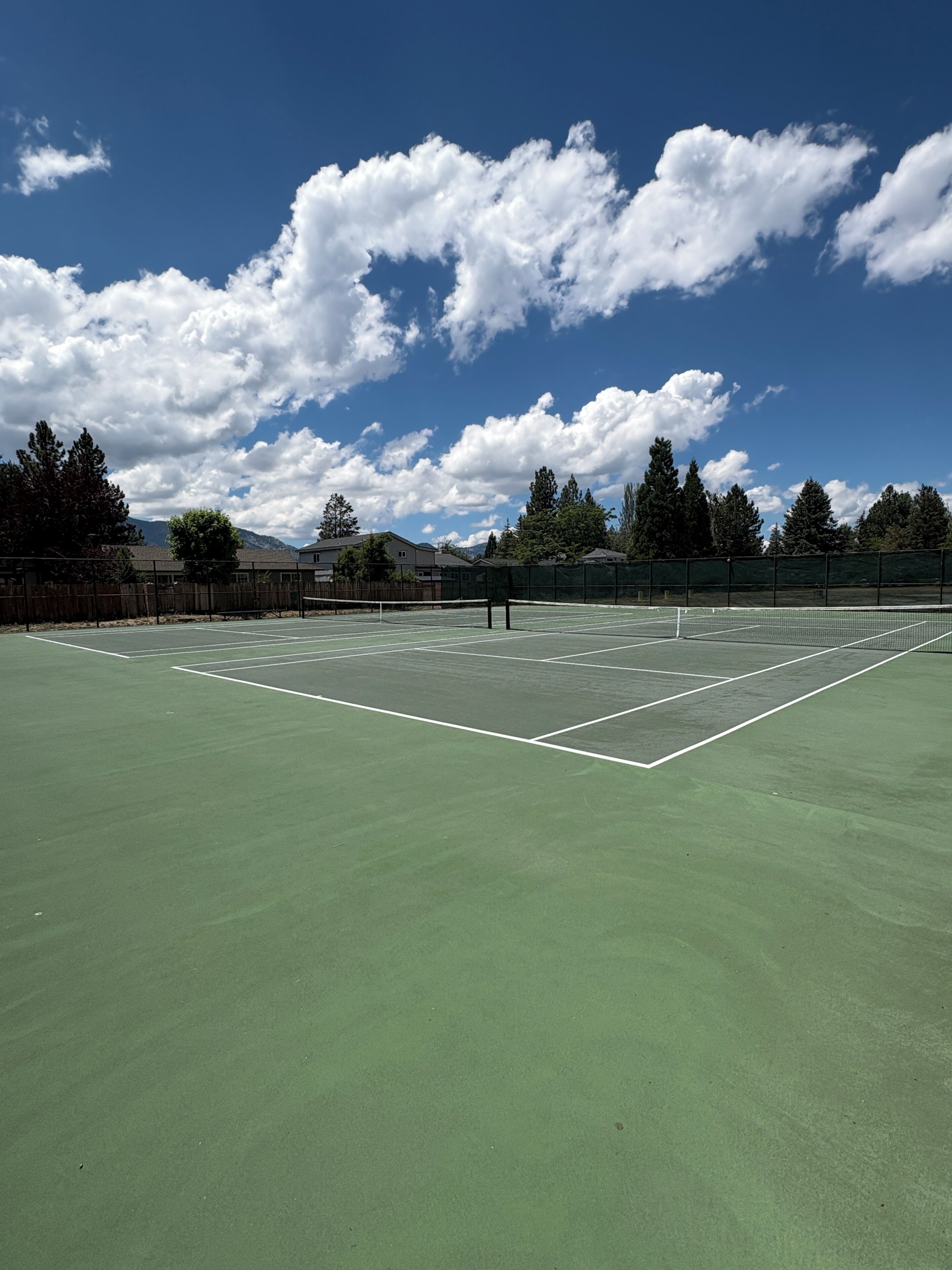 A tennis court with a net, surrounded by trees and buildings.