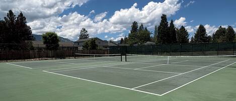 A tennis court with a net, surrounded by trees and buildings.