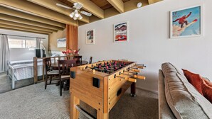 Une pièce avec une table de baby-foot, un canapé, un ventilateur de plafond et des œuvres d’art murales.